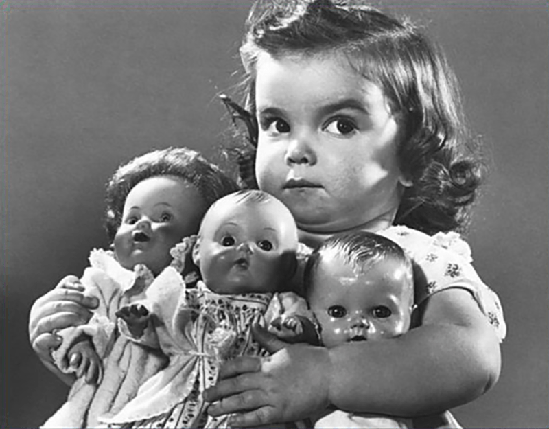 greedy little girl clutching three dolls angrily